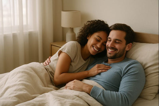 Happy couple lying close together in bed, smiling and relaxed, representing intimacy and emotional connection during a woman’s menstrual cycle.