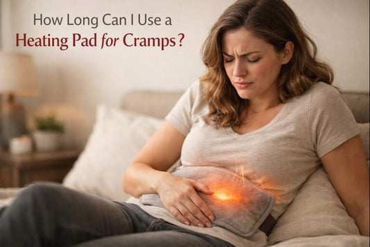 Woman using a heating pad for menstrual cramps while sitting on a bed, showing how long a heating pad can be used safely for period cramps and lower abdominal pain relief.
